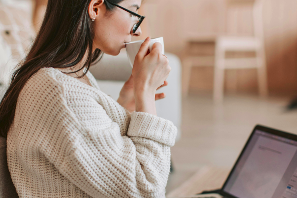 One woman with glasses drinking from a cup in front of a laptop